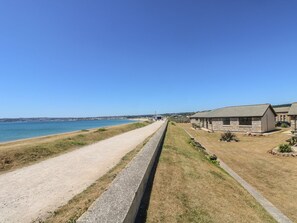 A coastal road leading to a row of stone buildings with a clear view of the sea. - Seabreeze (Penzance)