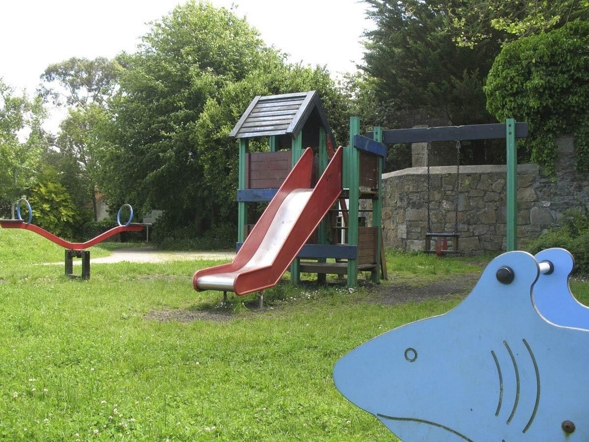 A playground with a red slide, a seesaw, and a climbing structure.