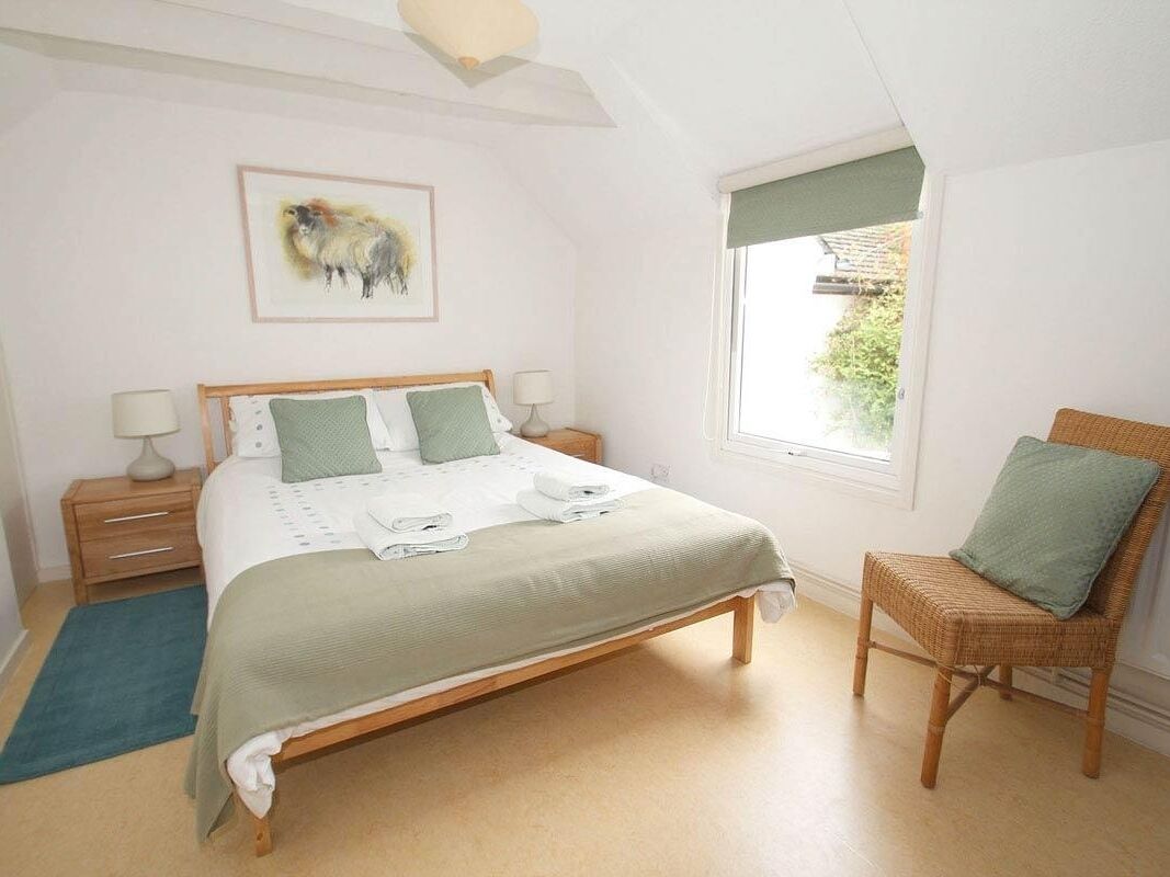 A bedroom with a bed, a chair, a nightstand, a lamp, and a window with a view of greenery.