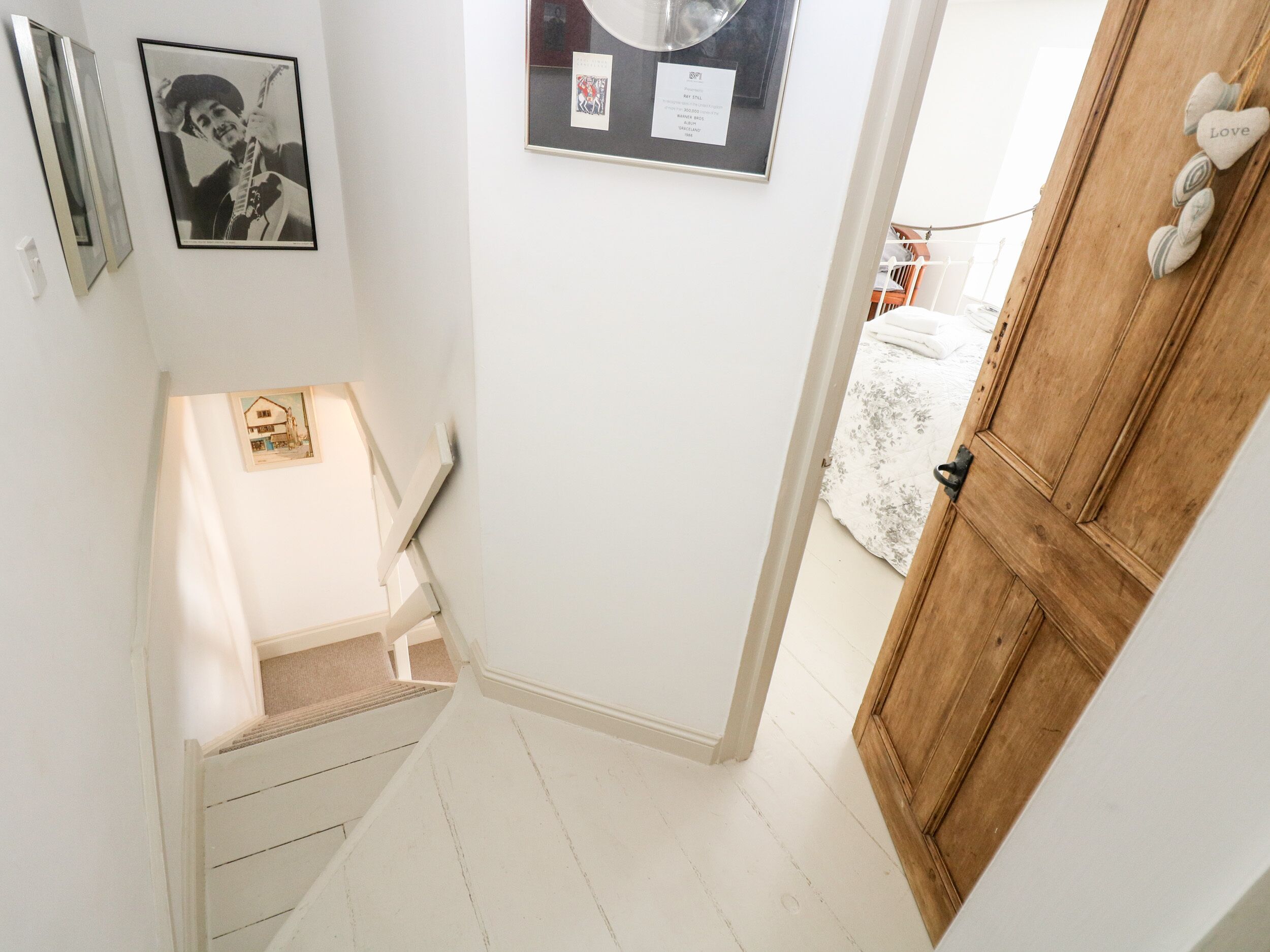 A narrow hallway with a wooden door, a white wall, and a framed picture.
