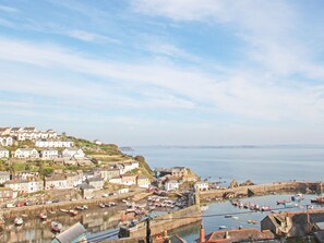 A coastal town with a harbor filled with boats, a fortified structure, and a hillside with buildings.