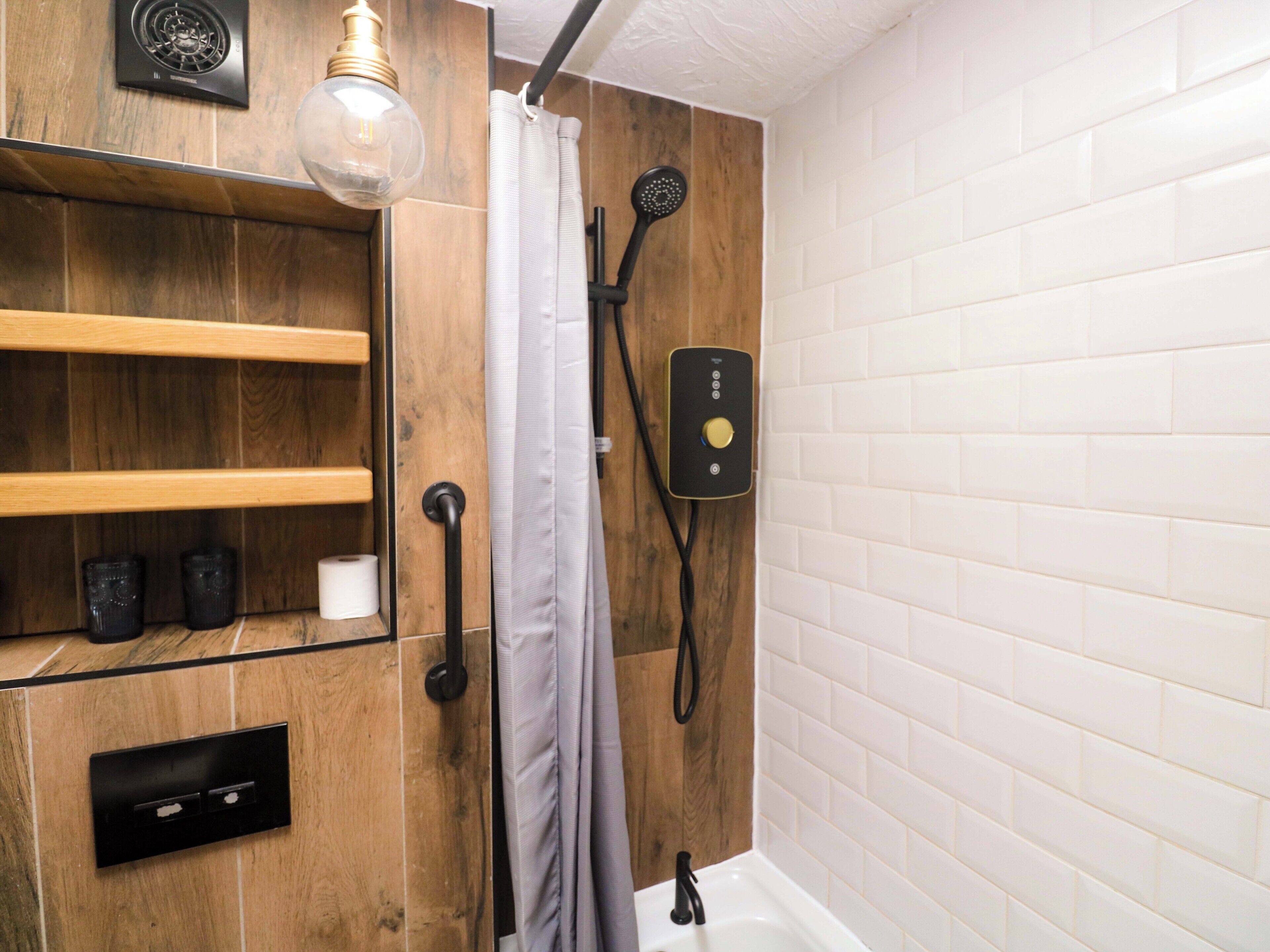 A bathroom with a wooden vanity, a shower with a handheld showerhead, and a light fixture.