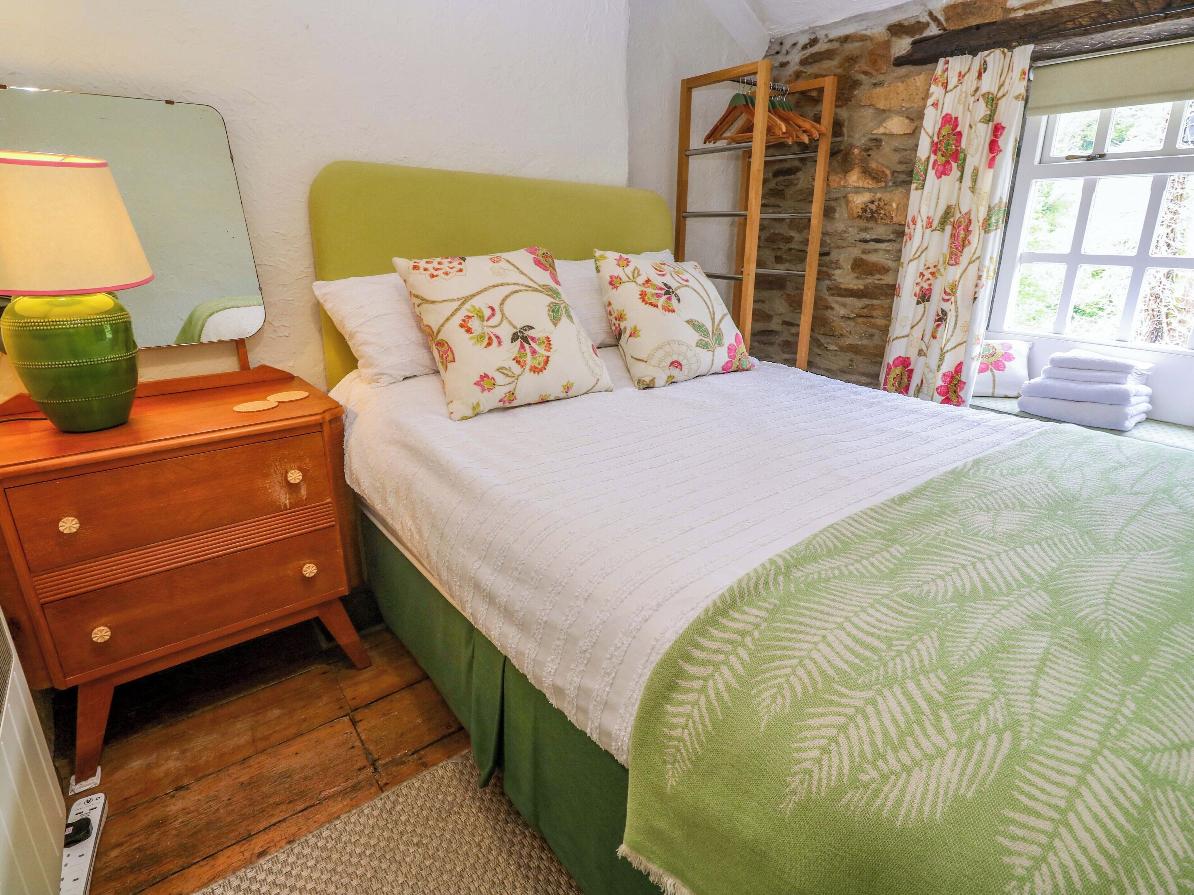 A bedroom with a wooden nightstand, a mirror, a green headboard, floral pillows, a white bedspread, and a green throw blanket.