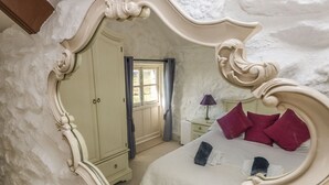 A bedroom with a large ornate mirror, a bed with pillows, a nightstand, and a dresser. - Boar's House (Penzance)