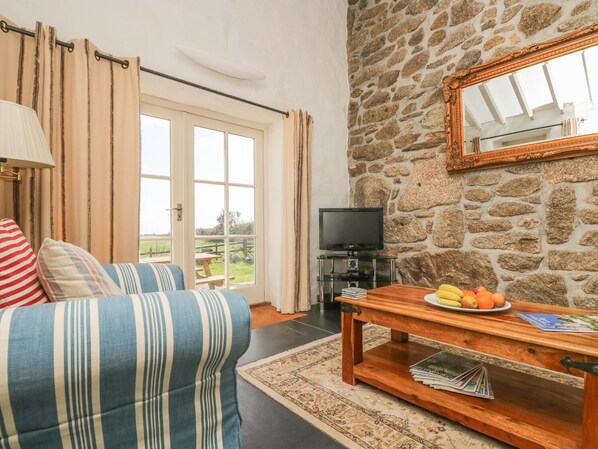 A living room with a stone wall, a television, a wooden table with fruit, and a striped sofa. - Boar's House (Penzance)