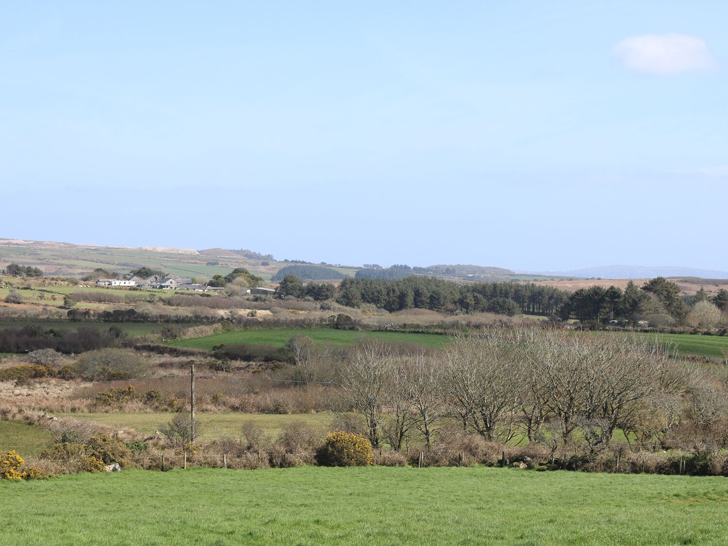A rural landscape with a house in the distance, surrounded by fields and trees.