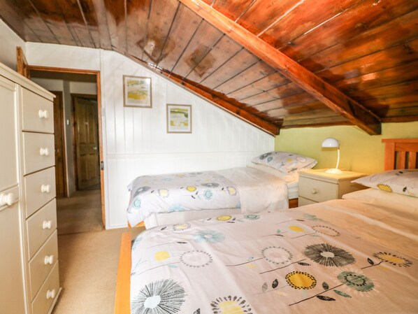 A bedroom with two beds, wooden ceiling beams, a dresser, and a nightstand with a lamp. - Chenalls Cottage (Helston)
