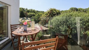 Un balcon avec une table et des chaises, un vase rempli de fleurs et un verre d’eau.