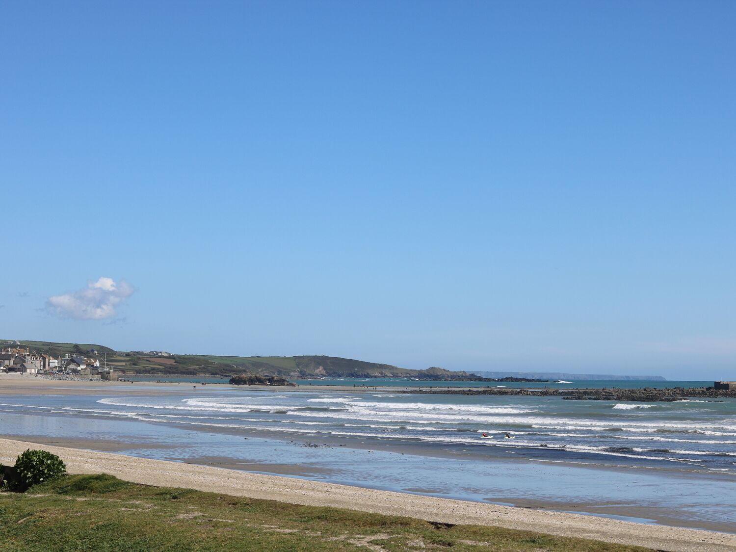 Une plage côtière, avec un ciel dégagé, des vagues et une ville qui se dessine à l'horizon.