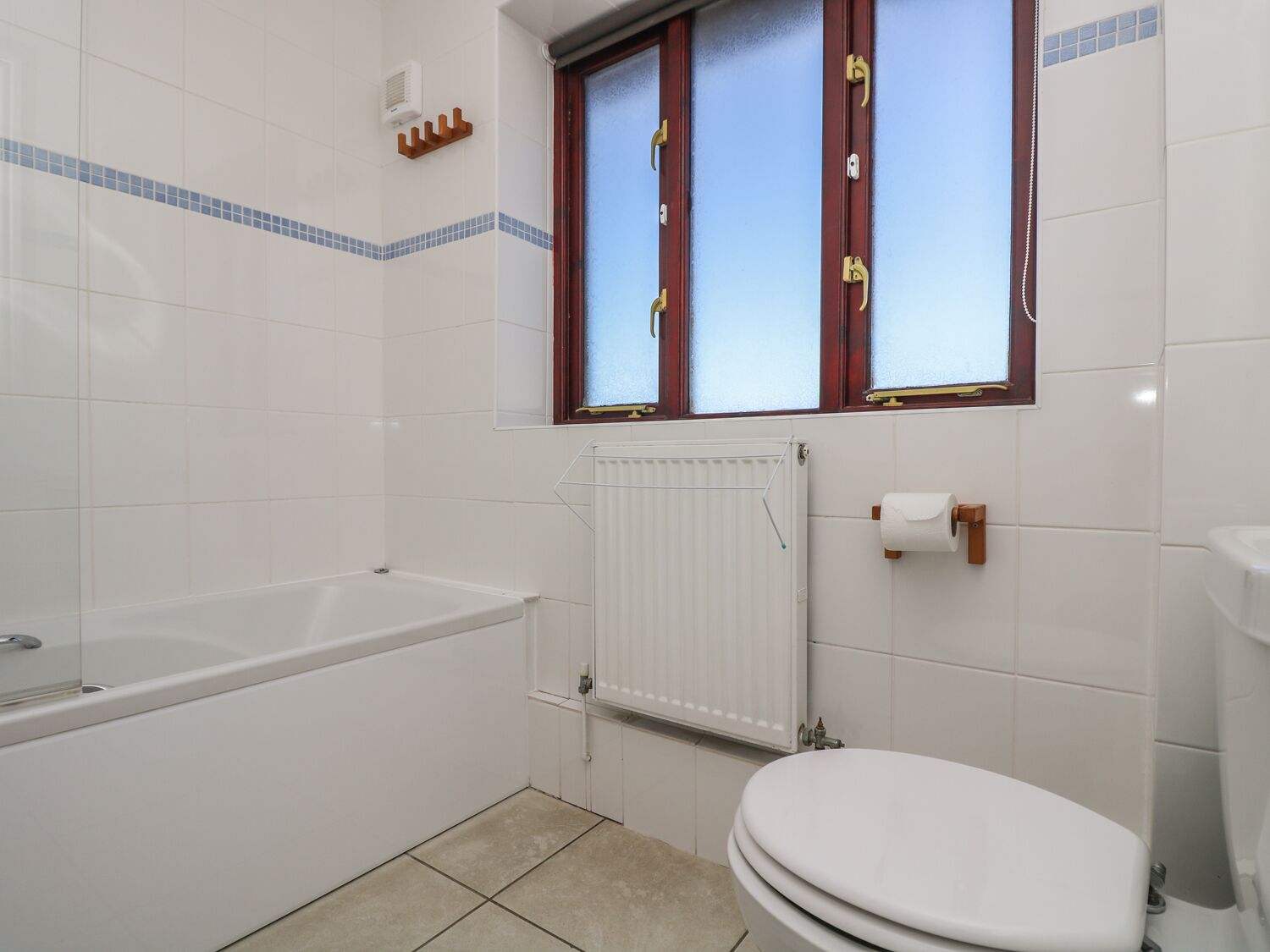 A bathroom with a bathtub, toilet, and a window with wooden frames.
