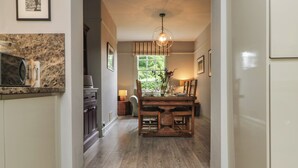 A kitchen with a wooden dining table, a hanging light fixture, and a window with a view of greenery. - Penwarne Lodge (Falmouth)