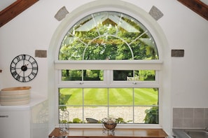 A kitchen with a large arched window, a wall clock, and a kitchen counter with a bread container.