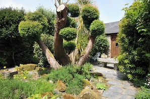 Ein Steinweg schlängelt sich durch einen Garten mit verschiedenen Pflanzen und einem Holzgebäude.