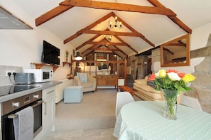 A cozy kitchen with a dining area, wooden beams, a chandelier, and a vase of flowers.