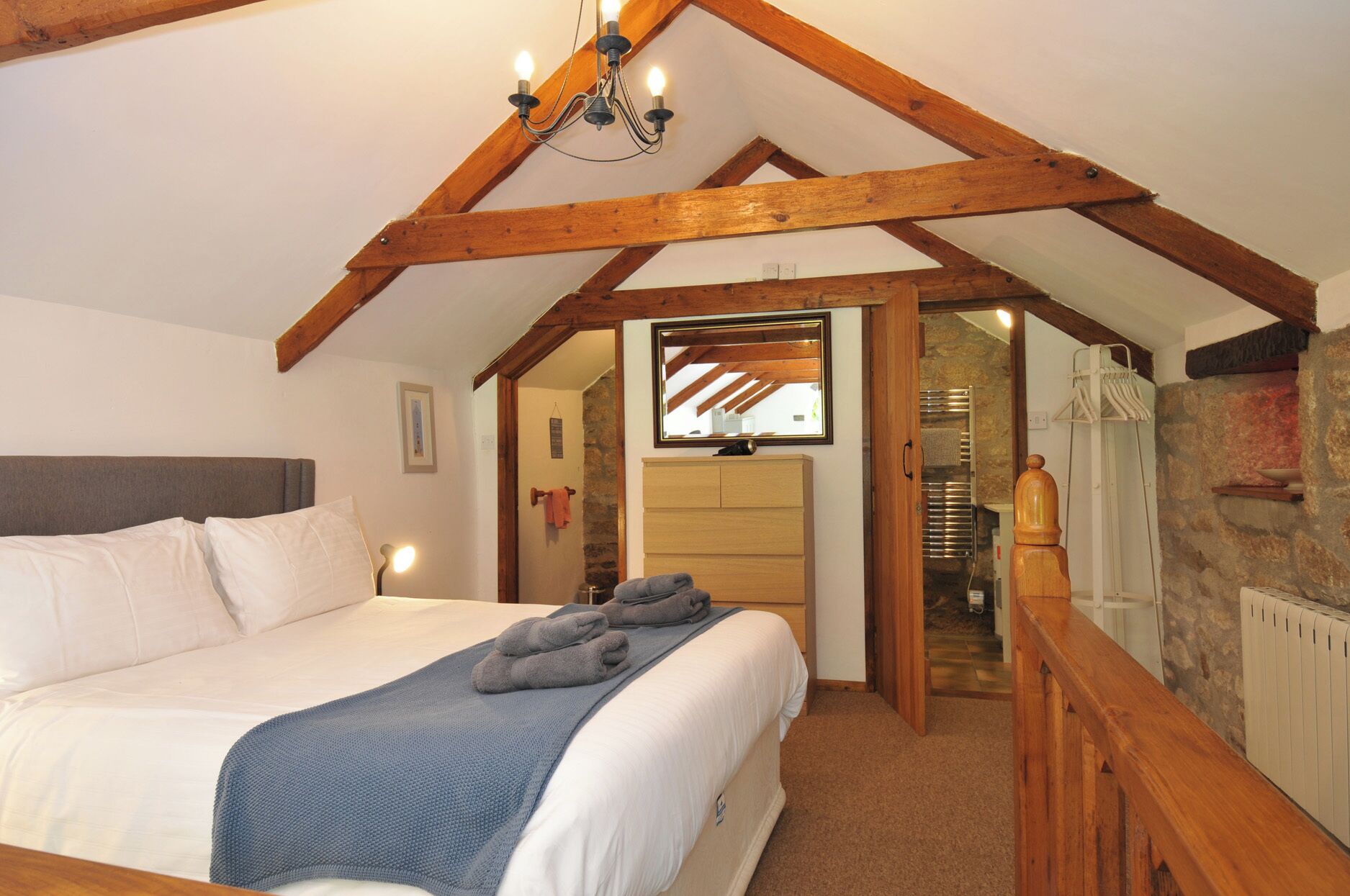 Una camera da letto con un letto, soffitto in legno, uno specchio, un comò e un muro in pietra.