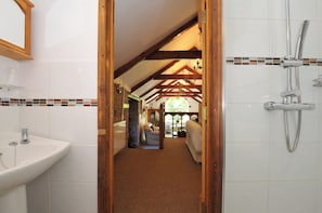 A bathroom with a shower, a sink, and a wooden-framed doorway leading to a living area.