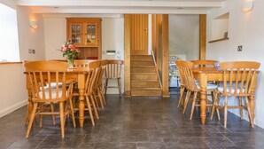 A dining area with a wooden table and chairs, a staircase leading to another room, and a kitchen area with wooden cabinets. - Carne Mill (Helston)