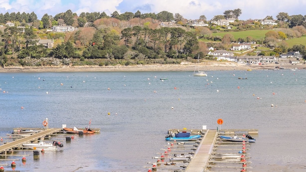 A coastal marina with boats docked, a pier, and houses in the background. - Carne Mill (Helston)