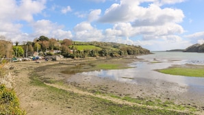 A coastal landscape with a sandy beach, a small harbor with boats, and houses on the hillside. - Carne Mill (Helston)