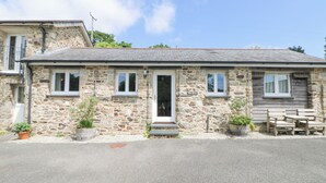 A stone building with a tiled roof, a wooden bench, and potted plants. - Byre (Lostwithiel)