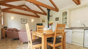 A cozy living room with a wooden dining table, chairs, a sofa, and a kitchen area with a dishwasher and sink. - Byre (Lostwithiel)