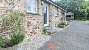 A stone building with a gravel driveway, a wooden bench, and a small shed in the background. - Byre (Lostwithiel)
