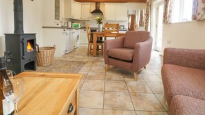 A cozy living room with a fireplace, a dining area, and a kitchen with white cabinets and a black stove. - Byre (Lostwithiel)