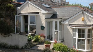 A two-story house with a garden entrance, a conservatory, and a small porch with wicker furniture. - Seabien (Falmouth)