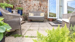 A stone wall patio with wicker furniture and potted plants. - Seabien (Falmouth)