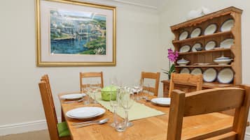 Comedor con mesa de madera dispuesta para cuatro, sillas, un cuadro enmarco y una estantería de cerámica.
