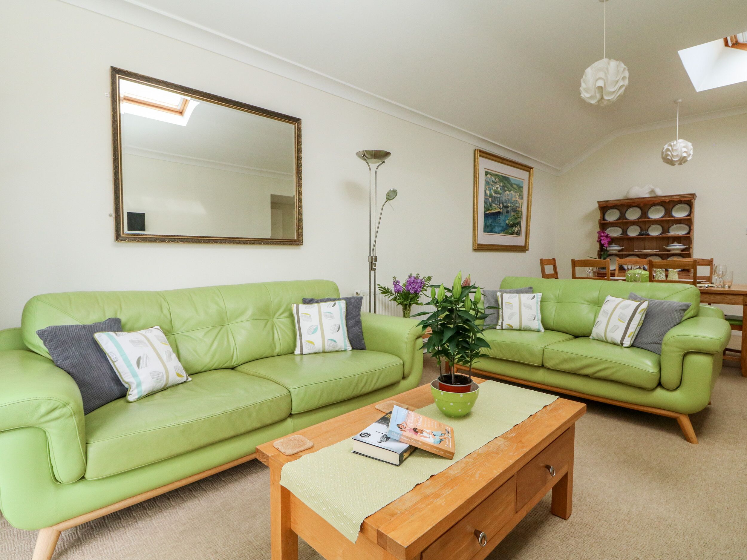 A living room with a green sofa, a wooden coffee table, a floor lamp, and a dining table with chairs.