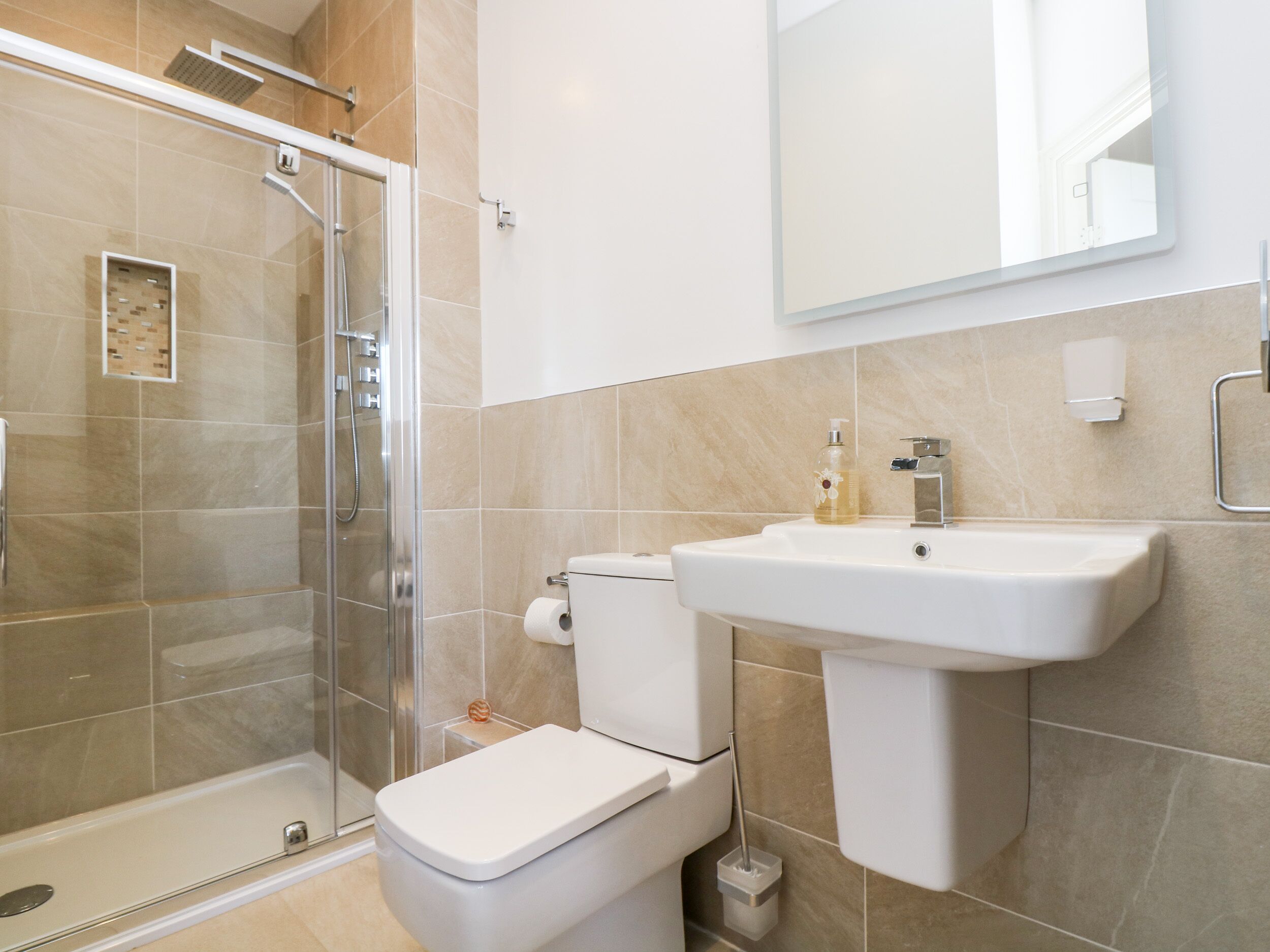 A modern bathroom with a glass-enclosed shower, a toilet, and a sink with a mirror above.