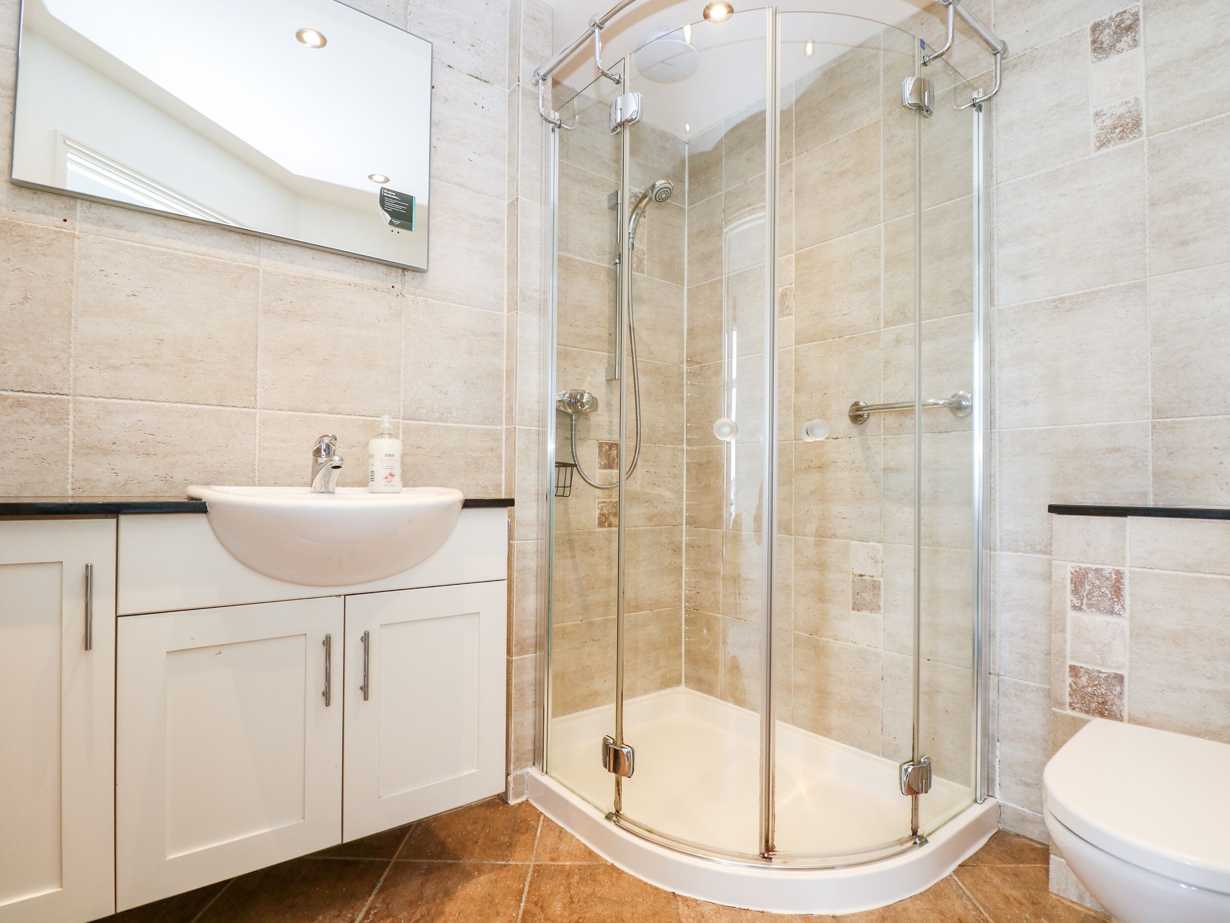 Un baño moderno con ducha de vidrio, lavamanos blanco y retrete.