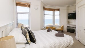 Une chambre à coucher avec un lit, deux fenêtres, un bureau, une chaise, une télévision et une vue sur la mer.