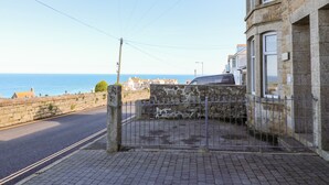 Un bâtiment en pierre avec un portail en métal, un trottoir pavé et une vue sur la mer.