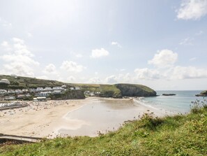 A coastal beach with houses along the cliffside, a sandy beach, and a calm sea.