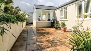 A narrow paved pathway leading to a conservatory with a glass roof, surrounded by potted plants and a beige wall. - Mynheer Farm Bowji (Redruth)