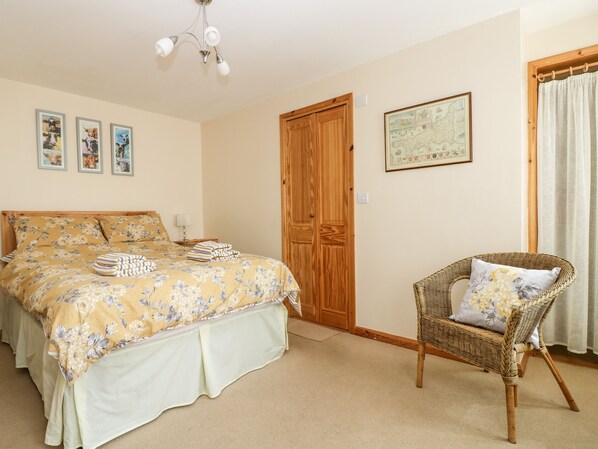 A bedroom with a bed, a wicker chair, a wooden door, and a map on the wall.