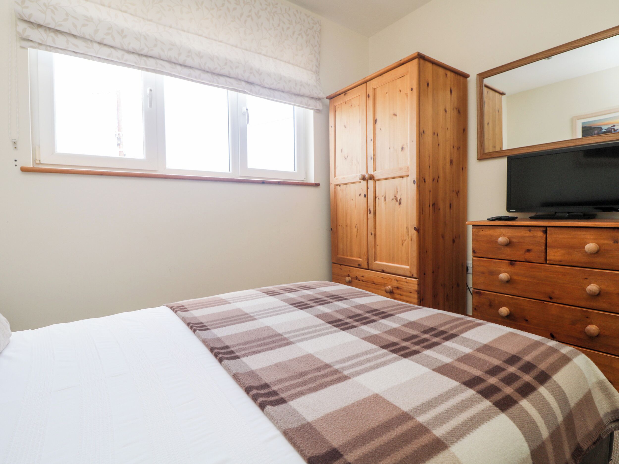 Una camera da letto con un letto, un'armadio in legno, una televisione su un comò e una finestra con persiana bianca.