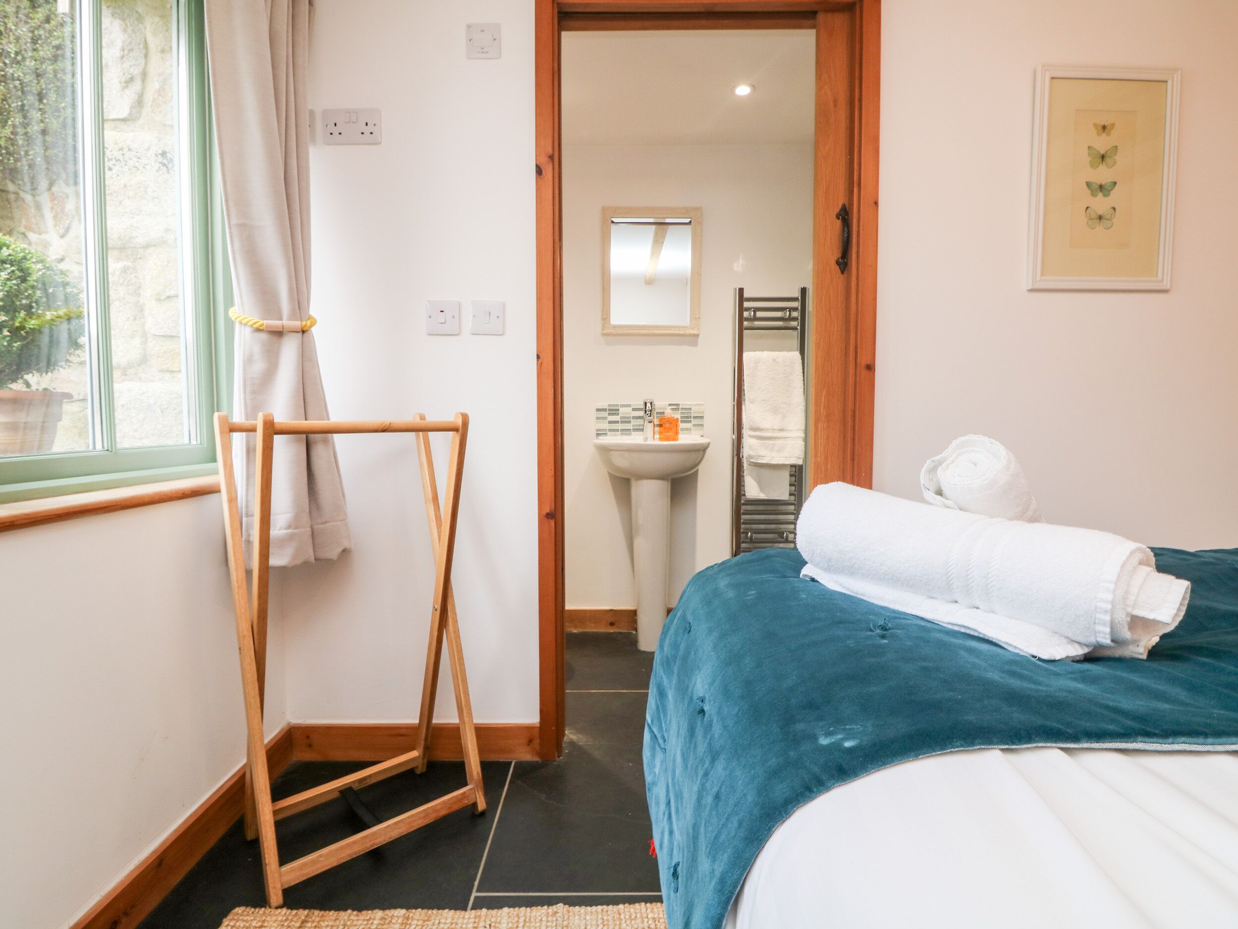 Un dormitorio con cama, un tendedero de madera, un lavamanos y un espejo.