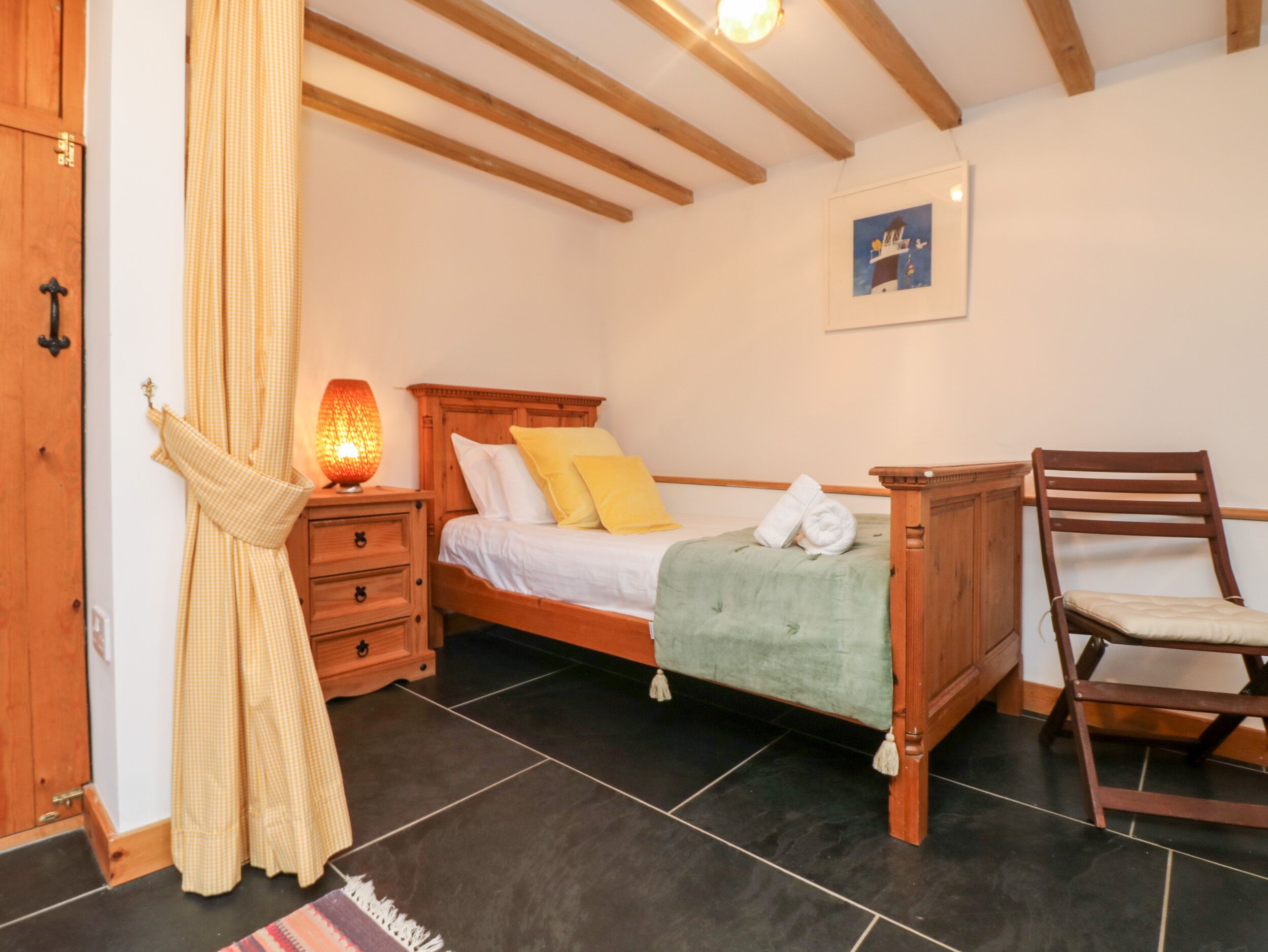 A bedroom with a wooden bed, a nightstand with a lamp, a chair, and a door.