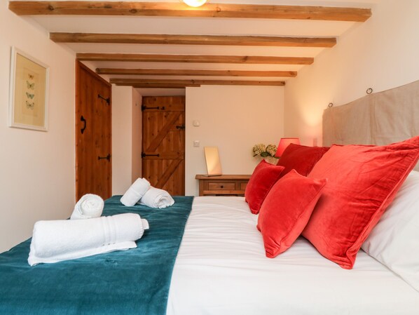 A bedroom with a bed, a wooden door, a nightstand, and a lamp. - Hay Loft (Camborne)