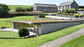 A stone building with a modern glass extension, surrounded by a well-maintained lawn and a stone wall. - Marhayes (Camelford)