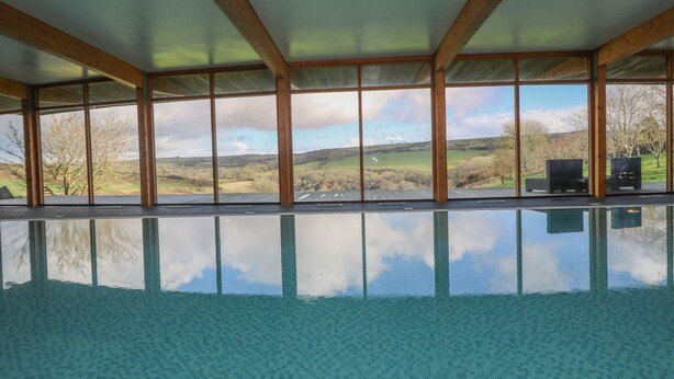 A large indoor swimming pool with a clear view of a rural landscape through large windows. - Marhayes (Camelford)