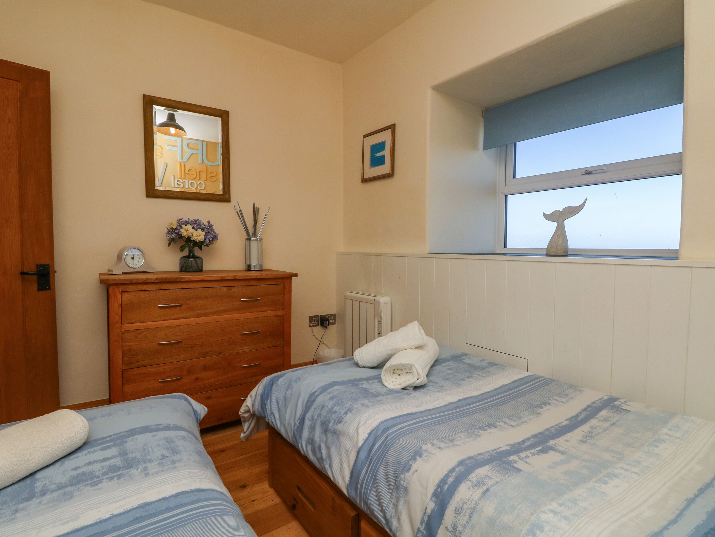 A bedroom with two beds, a dresser, a clock, and a window with a decorative item.