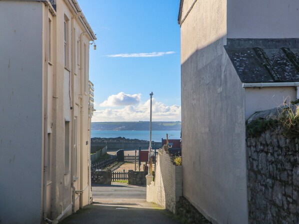 Un estrecho callejón con vista al mar y acantilados a lo lejos.