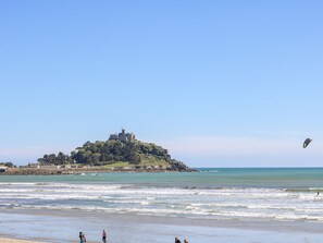 A beach with a castle on a hill, waves, and a kite in the sky. - Mackerel Sky (Marazion)