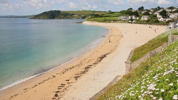 A beach with a sandy shore, a calm sea, and houses in the background. - Halvosso (Penryn)