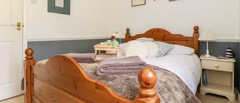 A bedroom with a wooden bed, a bedside table, a nightstand, and a wall-mounted lamp.