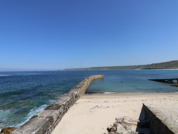 A coastal scene with a sandy beach, a stone wall, and a clear blue sky.